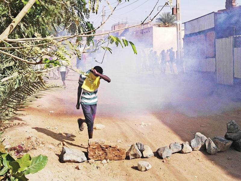 سوداني يحاول الاحتماء من قنبلة غاز مسيلة للدموع خلال تظاهرة في ضاحية بوري بالخرطوم (أ ف ب)