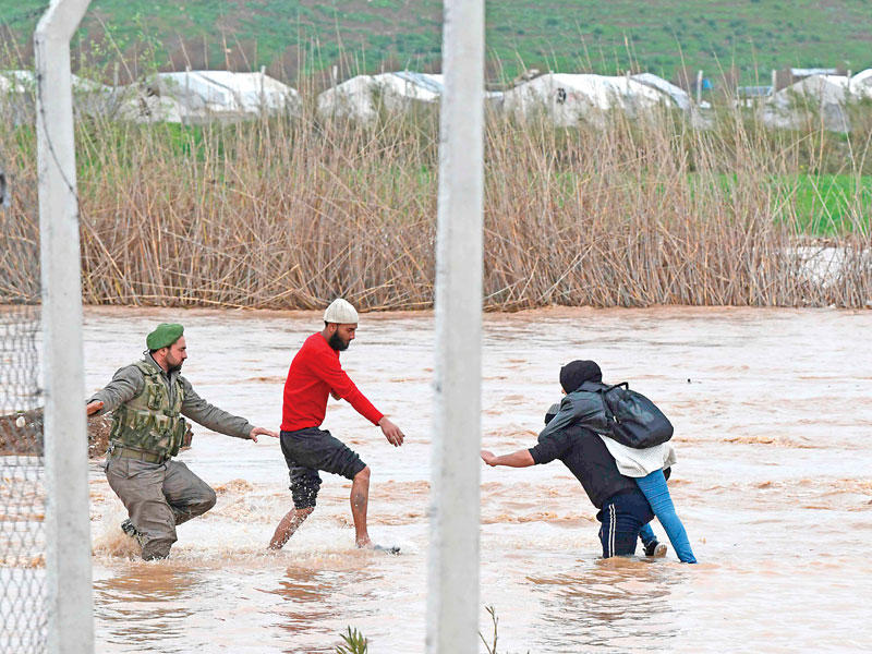 نازحون يعبرون منطقة غمرتها السيول بمخيم دير البلوط في ريف عفرين أمس الأول  (أ ف ب)