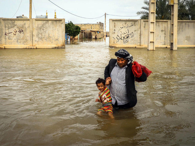 إيراني يحمل ابنه وسط مياه السيول في قرية تابعة للأهواز جنوب غرب إيران الأحد الماضي (إي بي أيه)n