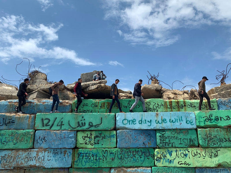 فلسطينيون يسيرون على جدار صد في ميناء غزة أمس (رويترز)n