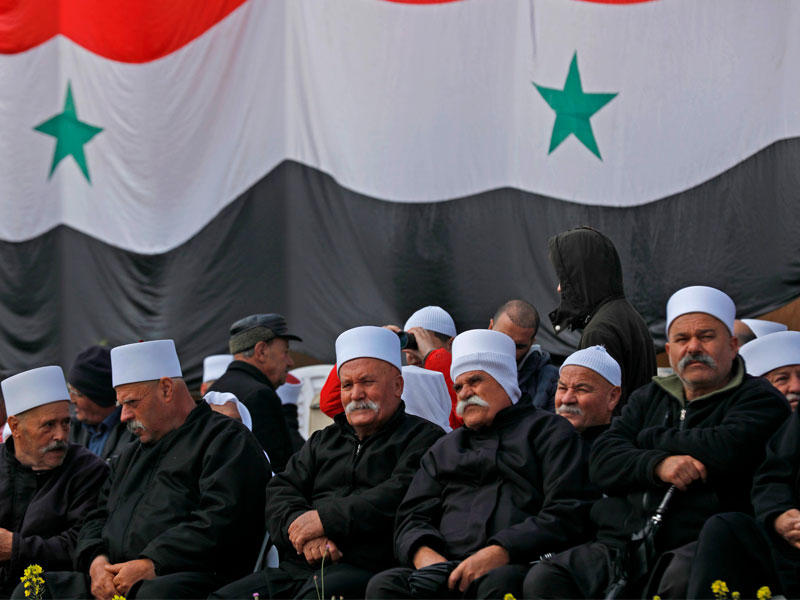  دروز أمام علم سوري كبير خلال تجمّع لهم في بلدة مجدل الشمس بالجولان أمس (أ ف ب)