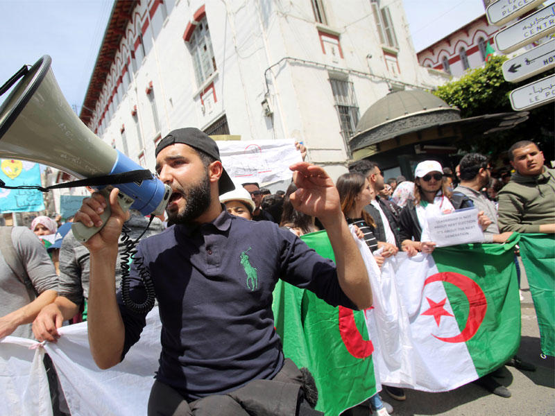 أحد المتظاهرين يصيح مكبرات الصوت بينما يحمل الآخرون الأعلام واللافتات أثناء الاحتجاجات المناهضة للحكومة في الجزائر العاصمة ، الجزائر