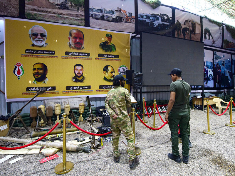 عنصران من «الحشد الشعبي» العراقي أمام صور لمقاتلين في «الحرس الثوري» الإيراني قتلوا بالعراق (إي بي أيه)