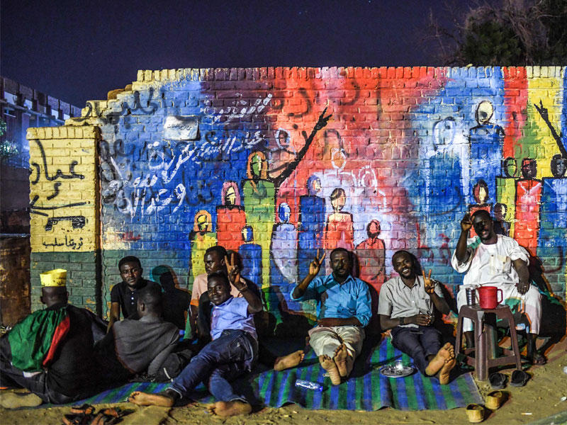 متظاهرون سودانيون يستريحون تحت رسمة غرافيتي قرب مقر القيادة العامة في الخرطوم أمس الأول t(أ ف ب)
