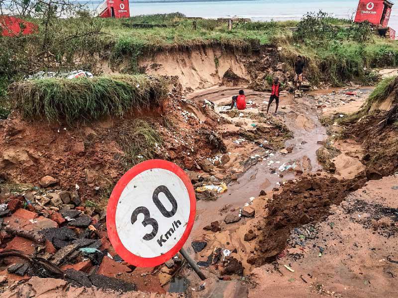 يقف السكان بجانب طريق دمرته الفيضانات جزئيًا بعد هطول أمطار غزيرة في بيمبا