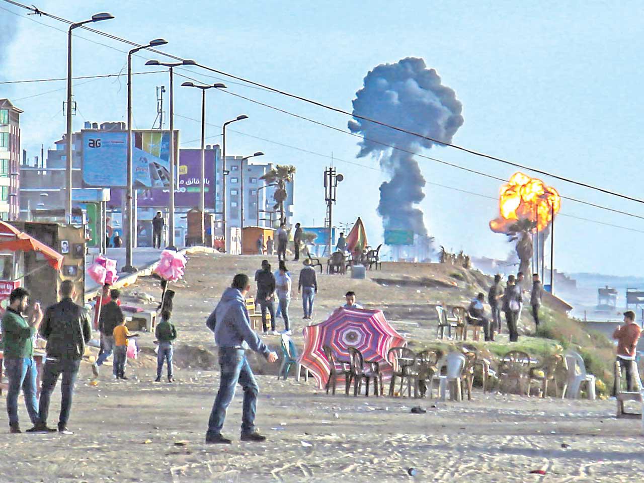 فلسطينيون على شاطئ غزة يراقبون النيران والدخان المتصاعد من القصف الإسرائيلي على غزة أمس الأول (أ ف ب)