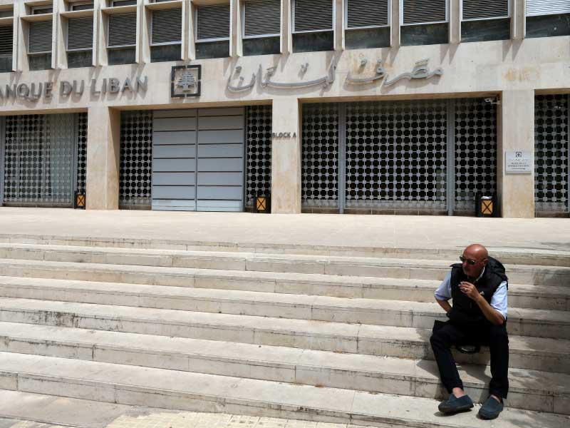 رجل يجلس أمام مصرف لبنان المركزي المقفل أمس (رويترز)