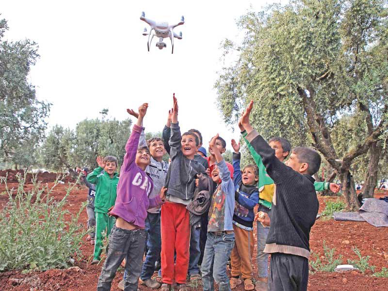 أطفال سوريون يلهون بطائرة مسيرة خلال اقامتهم في بستان زيتون في بلدة عتمة بعد فرارهم من مناطق القصف شمال غرب البلاد (أ ف ب) 