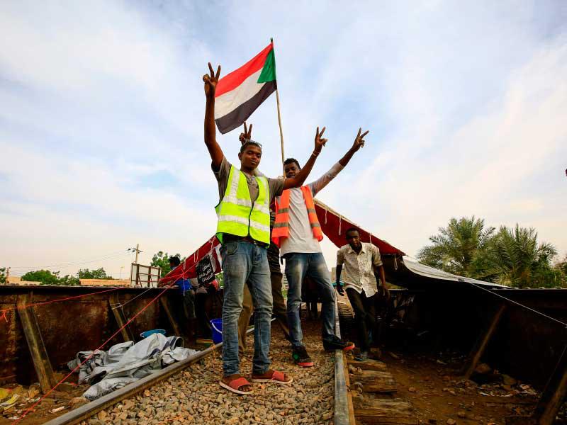 متظاهرون سودانيون يرتدون ملابس صفراء وينظمون لوحًا علميًا على منصة سكة حديد مغلقة تؤدي إلى موقع الاحتجاج في وسط الخرطوم