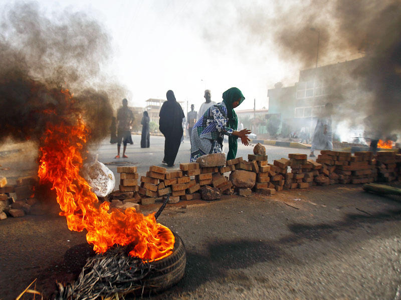 سودانية تشارك في إقفال أحد الطرق بالحجارة وسط إطارات مشتعلة في الخرطوم (أ ف ب)