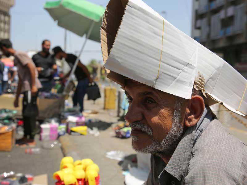 بائع متجول عراقي يحمي رأسه من أشعة الشمس باستخدام قطعة من الورق المقوى كقبعة خلال موجة الحر في العاصمة بغداد