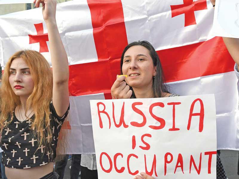 لافتة كتب عليها «روسيا هي المحتل» ترفعها متظاهرة أمام البرلمان في تبليسي أمس الأول  (أ ف ب)