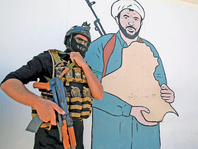 عنصر من «الحشد» أمام جدارية لرجل دين شيعي مسلح في النجف أمس t(رويترز)