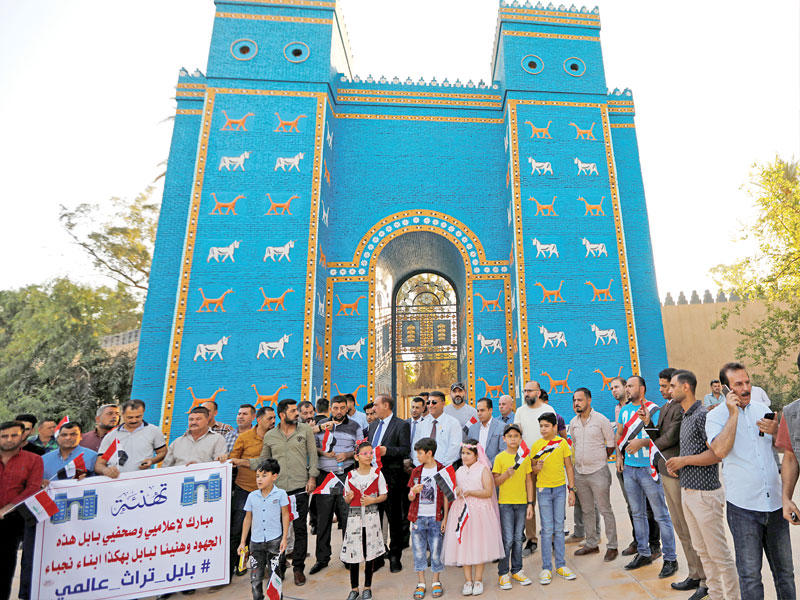 عراقيون يحتفلون بإدراج اليونسكو بابل على قائمة التراث العالمي أمام مجسم لبوابة عشتار التاريخية (رويترز)