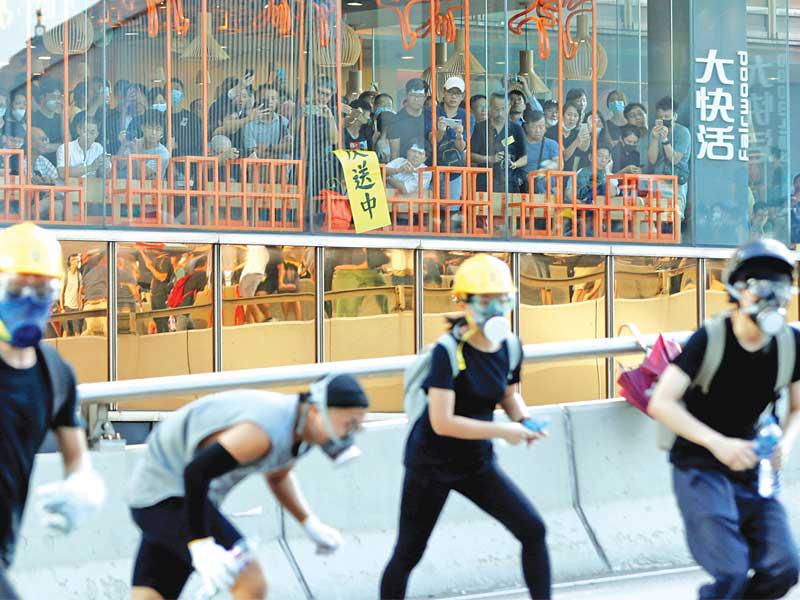 أشخاص داخل مطعم يراقبون متظاهرين في مواجهة الشرطة بهونغ كونغ أمسt(رويترز)