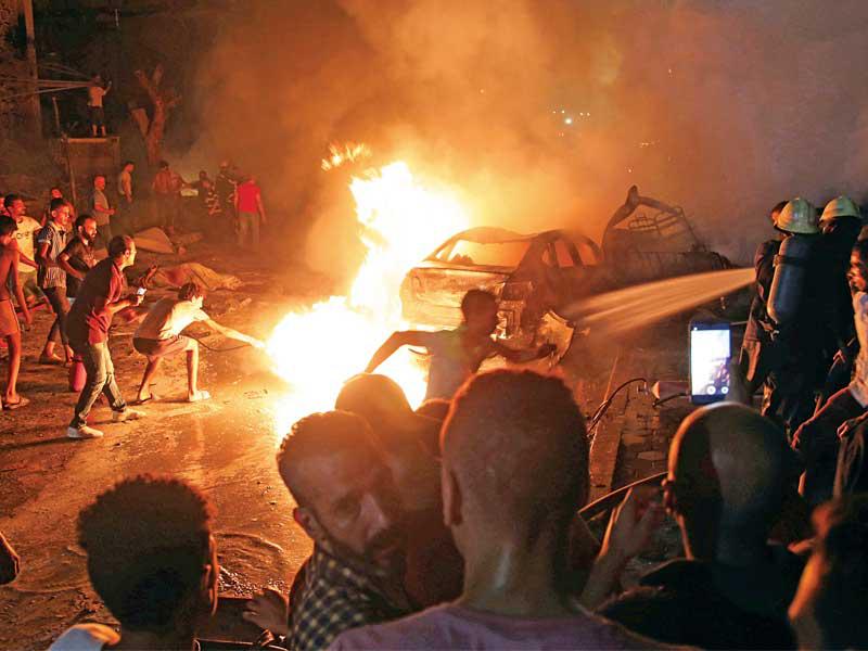 مصريون متجمّعون قرب سيارة تلتهمها النيران أمام معهد الأورام في القاهرة مساء أمس الأول (رويترز)