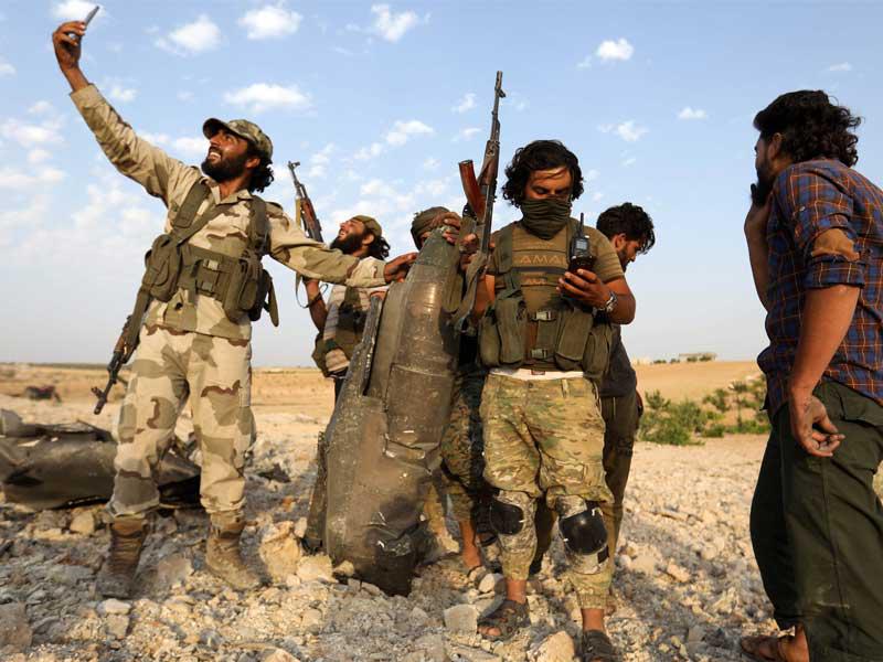 مقاتل من المعارضة يلتقط صورة مع حطام «السوخوي» في خان شيخون أمس الأول (أ ف ب)