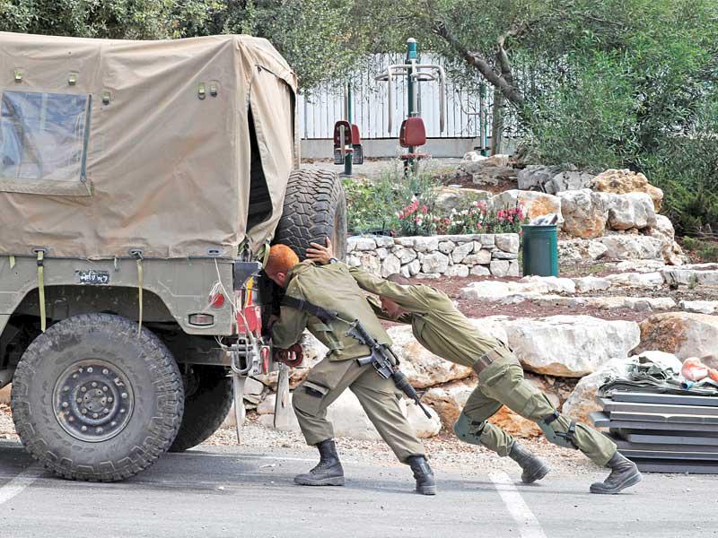 جنديان إسرائيليان يدفعان عربة عسكرية تعطّلت على حدود لبنان أمس (رويترز)