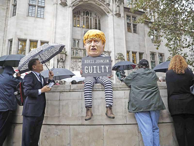 متظاهر يلبس قناعاً لجونسون ويحمل لافتة كتب عليها «مذنب» خارج مبنى المحكمة العليا في لندن أمس (أ ف ب)