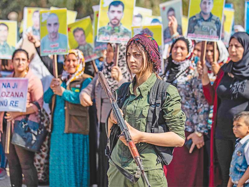 مقاتلة كردية تؤمن محتجين على استبعاد مناطقهم من لجنة الدستور أمام مقر الأمم المتحدة في القامشلي أمس (أ ف ب)n