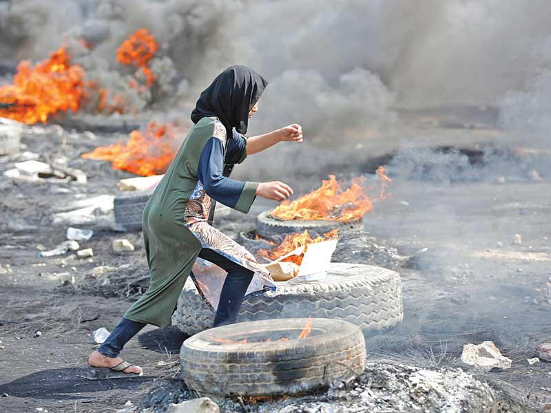 متظاهرة تركض بين الإطارات المحترقة وسط بغداد أمس (رويترز)
