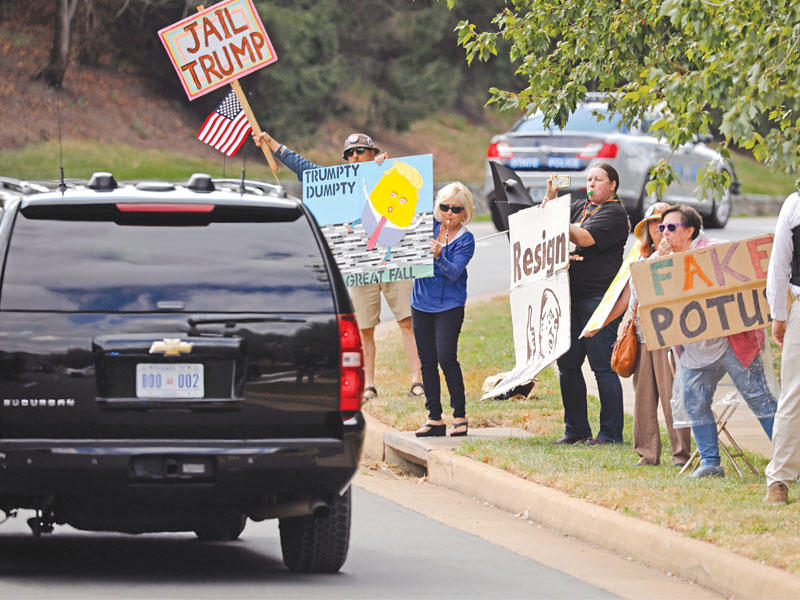 متظاهرون يرفعون لافتات تدعو إلى سجن ترامب خلال مرور موكبه في فرجينيا أمس الأول (اي بي ايه)