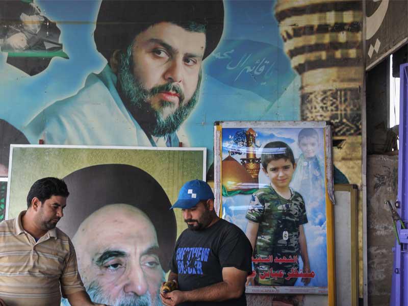 رجال عراقيون يعملون أمام ملصقات تحمل صور رجل الدين العراقي والزعيم السياسي مقتدى الصدر