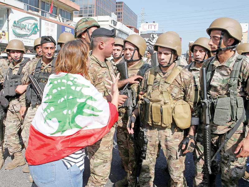 سيدة تلفّ نفسها بالعلم اللبناني أمام قوة من الجيش خلال إبعاد المتظاهرين من وسط الطريق في منطقة زوق مصبح أمسtttttt   (أ ف ب)