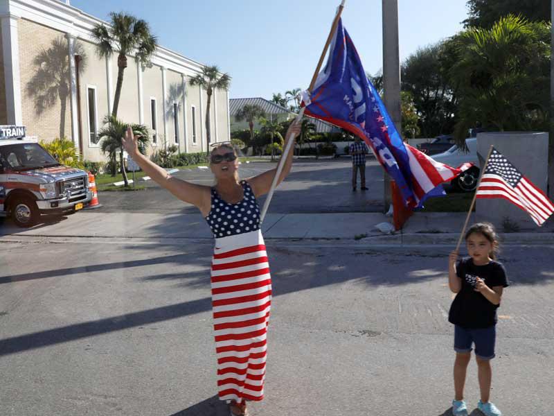 مؤيدة لترامب وابنتها ترفعان الأعلام الأميركية خلال مرور موكبه أمس الأول في بالم بيتش بفلوريدا (رويترز)