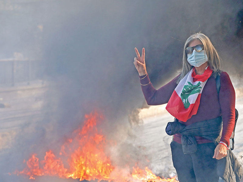 متظاهرة لبنانية ترفع شارة النصر قرب إطارات مشتعلة تغلق طريقاً في بيروت (أ ف ب)