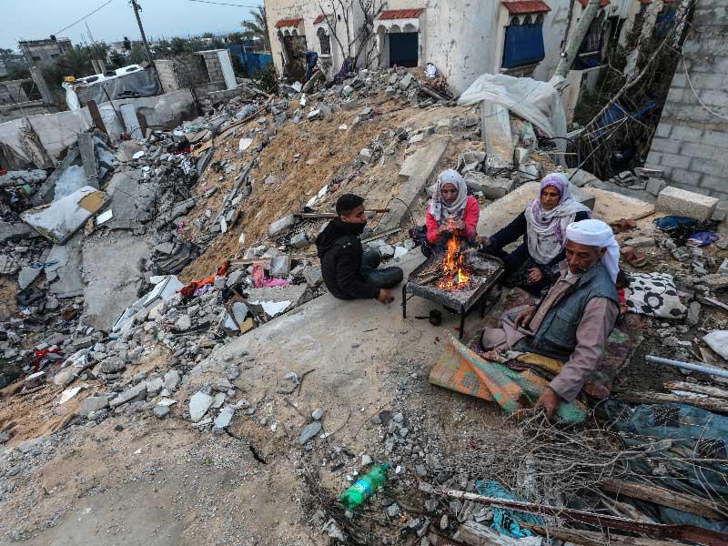 عائلة تجلس حول النار بين أنقاض منزلهم المدمر في بلدة خان يونس في قطاع غزة