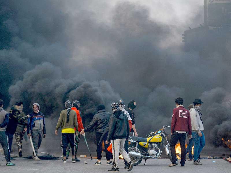 المتظاهرون المناهضون للحكومة يقفون أمام دخان الإطارات عند حاجز أمامي أثناء مظاهرة في مدينة النجف