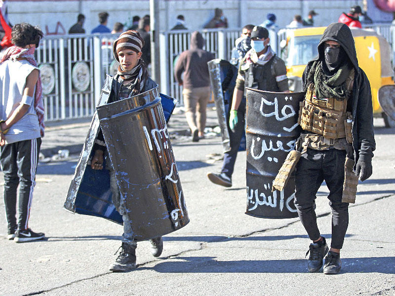 متظاهران يحملان دروعا مبتكرة خلال احتجاجات في ساحة الخلاني ببغداد أمس الأول (أ ف ب)