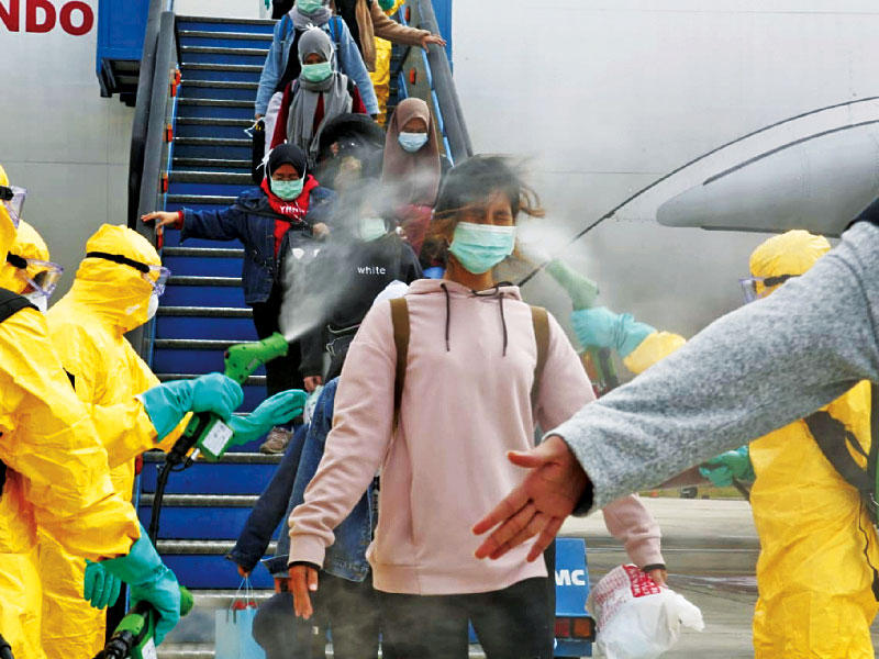 موظفون في مطار إندونيسي يعقمون أمس مسافرين قادمين من الصين قبيل عزلهم في قاعدة عسكرية (رويترز)