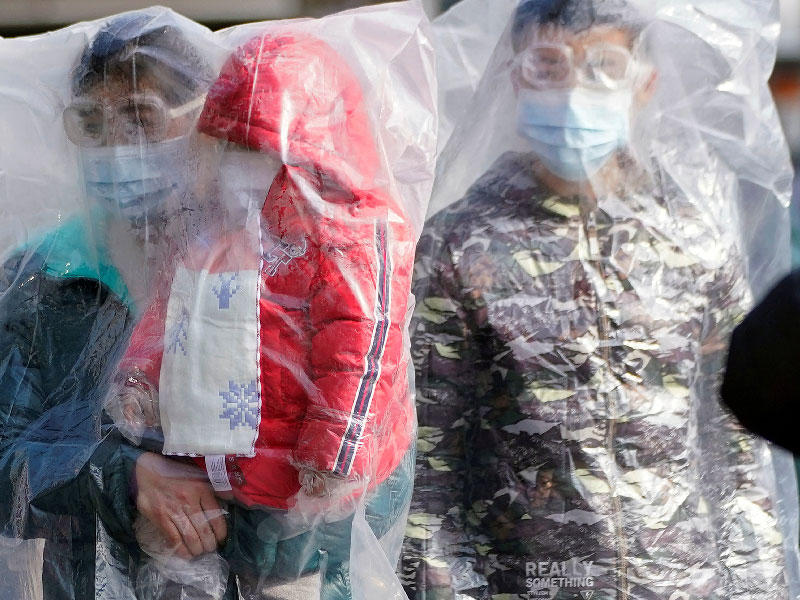 الركاب يرتدون أقنعة ومغطاة بأكياس بلاستيكية يسيرون خارج محطة سكة حديد شانغهاي