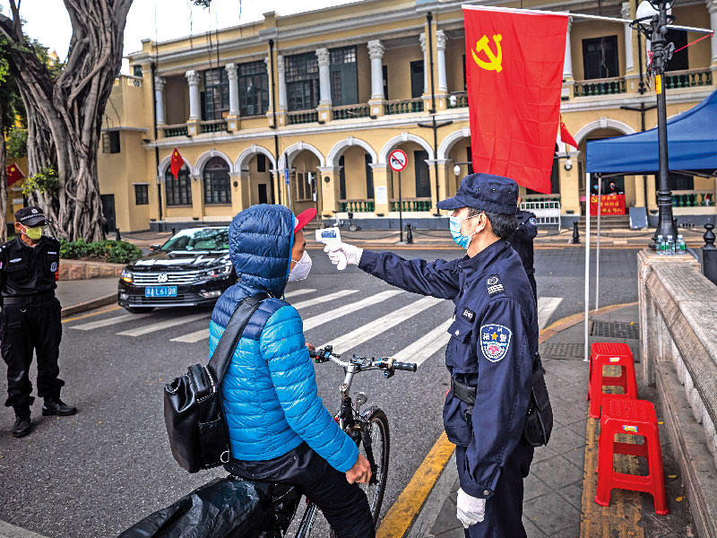  شرطي يفحص حرارة احد المارة في نقطة تفتيش بأحد شوارع مدينة غوانغزو الصينية أمس (ا ف ب)
