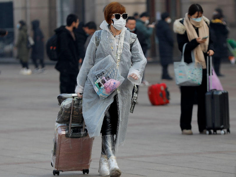 راكبة ترتدي قناعًا واقيًا ومعطفا بلاستيكيا كوقاية من فيروس كورون في محطة بكين