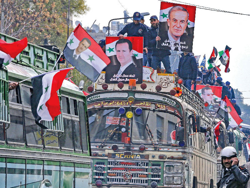 عمال يحملون الأعلام وصور الأسد ووالده في طريقهم لحضور المؤتمر السابع والعشرين لاتحادهم العام في دمشق أمس (أ ف ب)