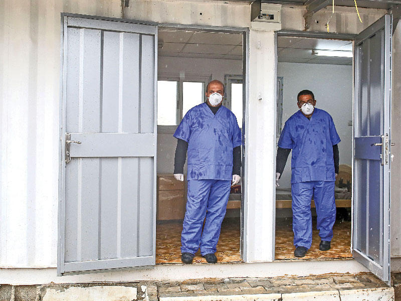 عاملان صحيان فلسطينيان في منطقة حجر صحي أقيمت على معبر رفح مع مصر (أ ف ب)