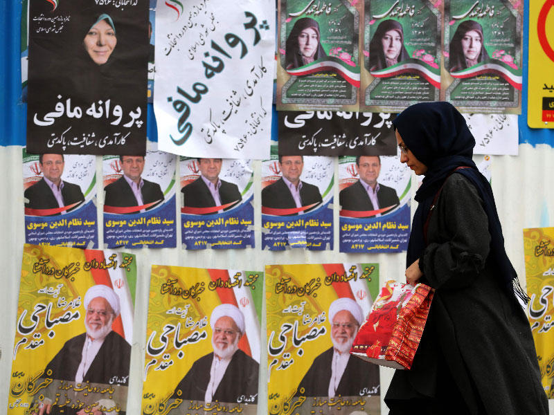 امرأة إيرانية تسير بجانب الملصقات والرايات الانتخابية خلال اليوم الأخير من الحملة الانتخابية في العاصمة طهران