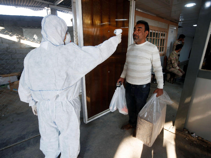 موظف عراقي يفحص درجة حرارة الراكب ، لدى وصوله إلى معبر الشلامجة الحدودي بين العراق وإيران