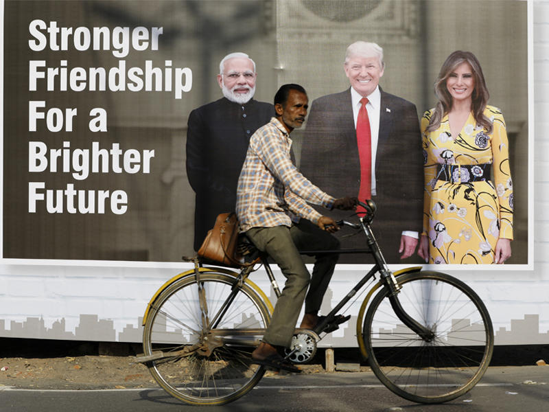هندي على دراجته الهوائية في مدينة أحمد آباد يمرّ أمام لوحة لترامب وزوجته ورئيس الوزراء الهندي أمس (رويترز)