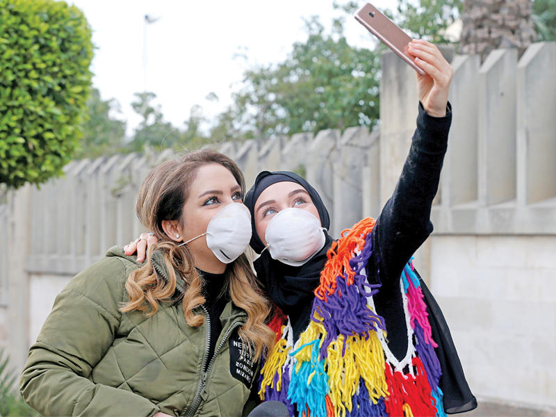 لبنانيتان بالأقنعة تلتقطان «سيلفي» أمام «مستشفى رفيق الحريري» أمس الأول (رويترز)