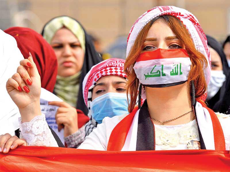 متظاهرة عراقية بكمامة تحمل علم العراق في النجف أمس (أ ف ب)