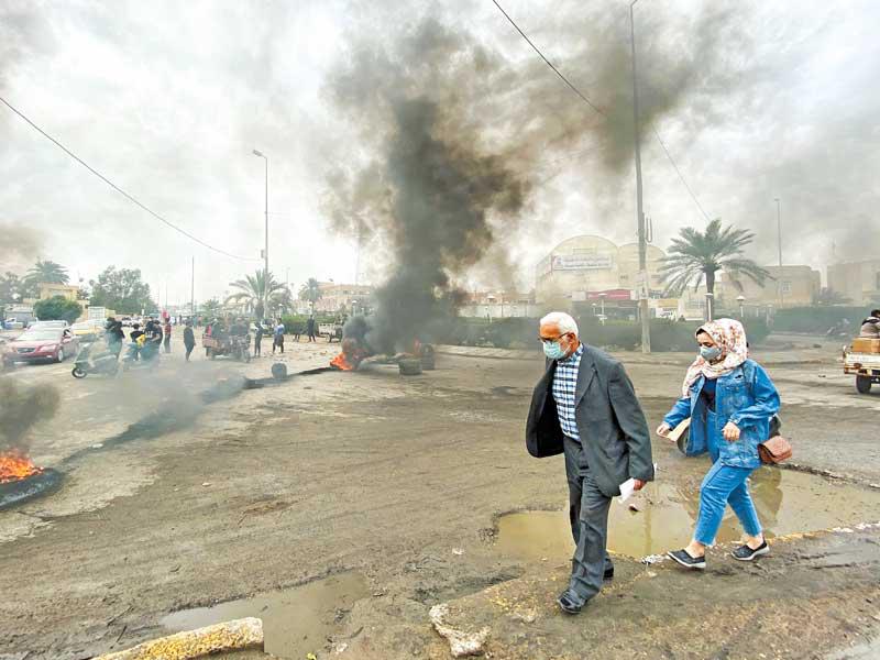 عراقيان يضعان كمامتين يمران أمام نقطة احتجاج في الناصرية أمس (رويترز) 