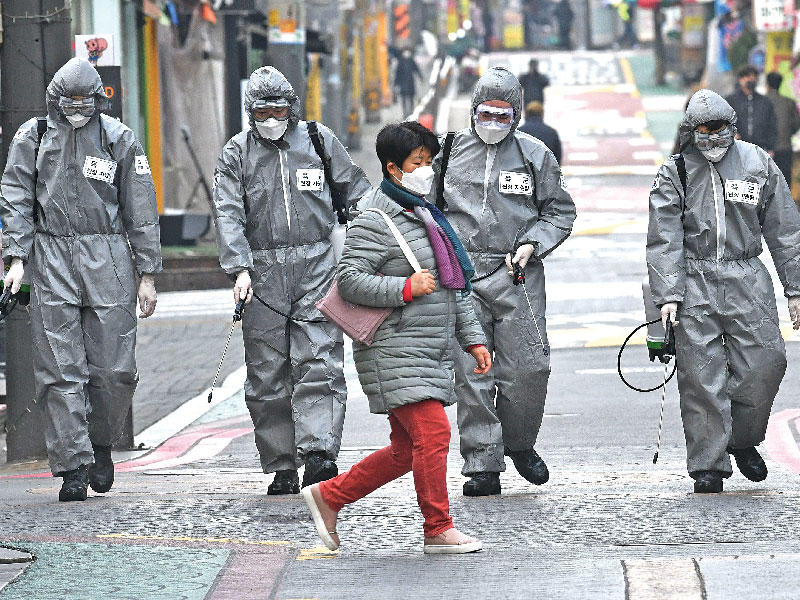 سيدة تمر أمام عناصر من الجيش يعقمون الطريق في سيول أمس (أ ف ب) 