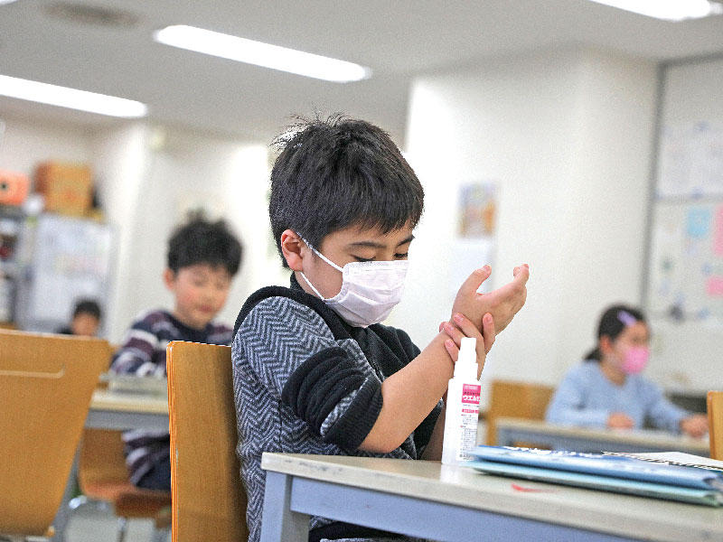 طفل ياباني يضع قناعاً  ويعقم يديه في حضانة بطوكيو أمس (رويترز)