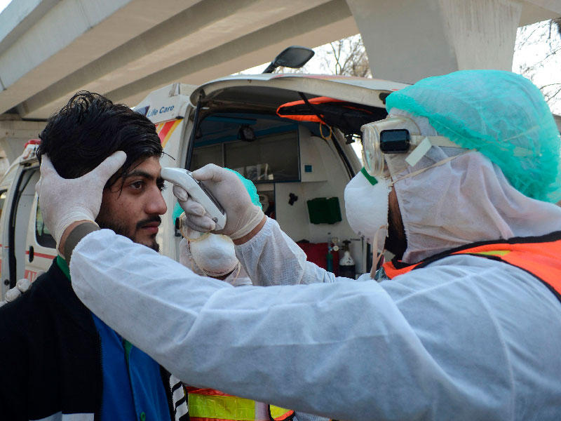 أحد رجال الإنقاذ الباكستانيين بفحص درجة حرارة رجل خلال تمرين تدبيري