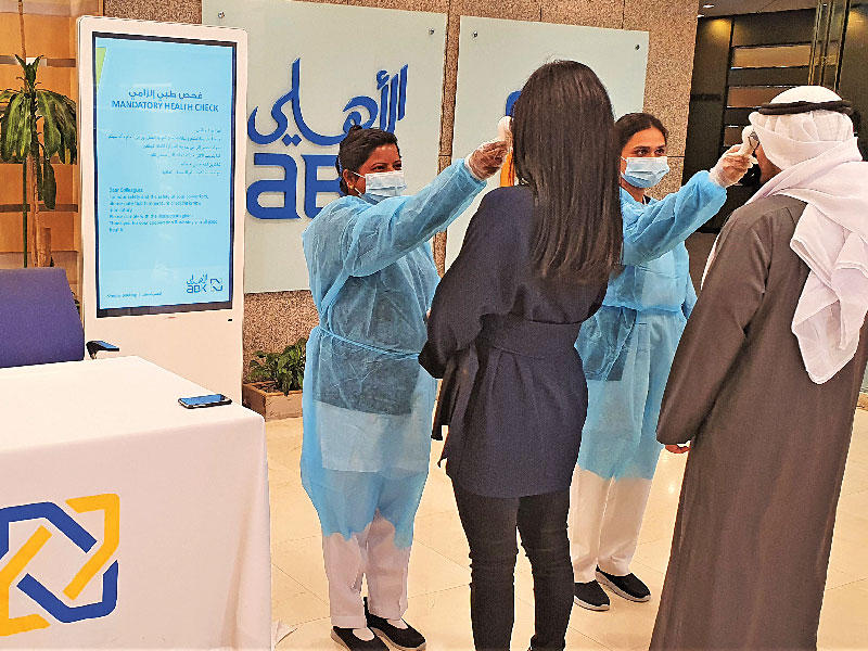 موظفو البنك الأهلي الكويتي أثناء فحص درجة الحرارة من طاقم «غلوبال كير» 