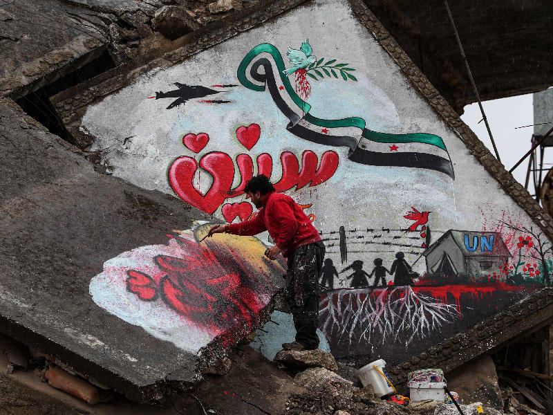 سوري يرسم على أنقاض مبنى مدمر في بنش بإدلب (أ ف ب)